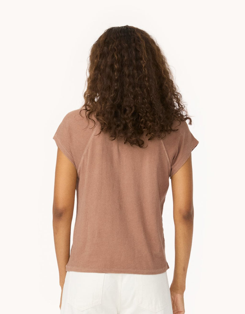 Back view of a woman wearing a cappuccino brown raglan t-shirt and white jeans on a white background