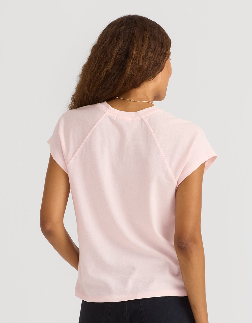 Back view of a woman wearing a light pink t-shirt on a plain background