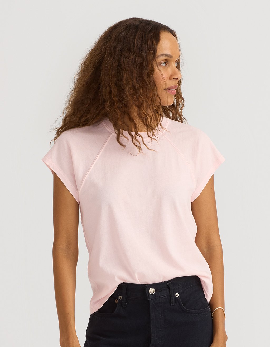 Woman wearing a light pink t-shirt and black jeans on a plain background
