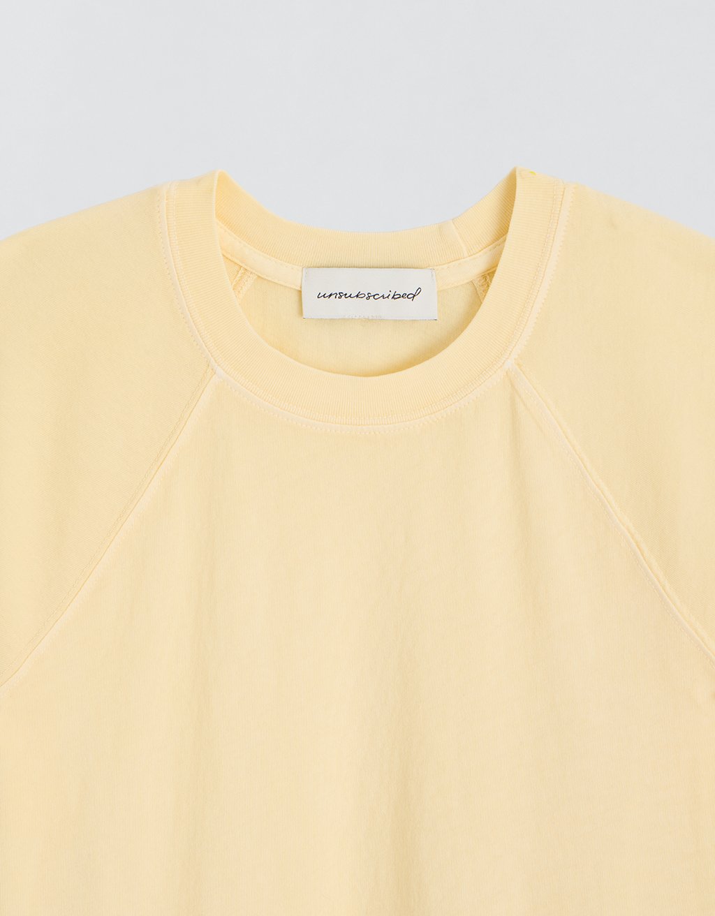Close-up of a yellow t-shirt with a brand label on a light gray background