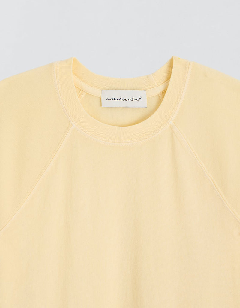 Close-up of a yellow t-shirt with a brand label on a light gray background