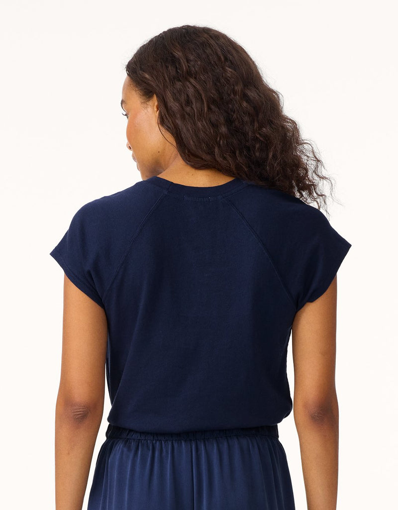 Back view of a woman wearing a navy blue raglan t-shirt and skirt on a white background