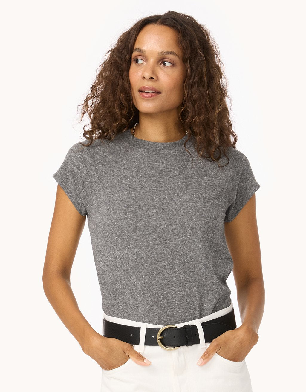 Woman wearing a heather gray raglan t-shirt and white pants with a black belt on a white background