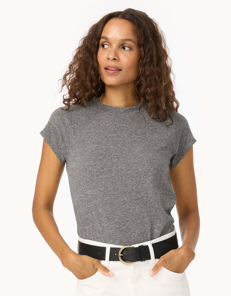 Woman wearing a heather gray raglan t-shirt and white pants with a black belt on a white background