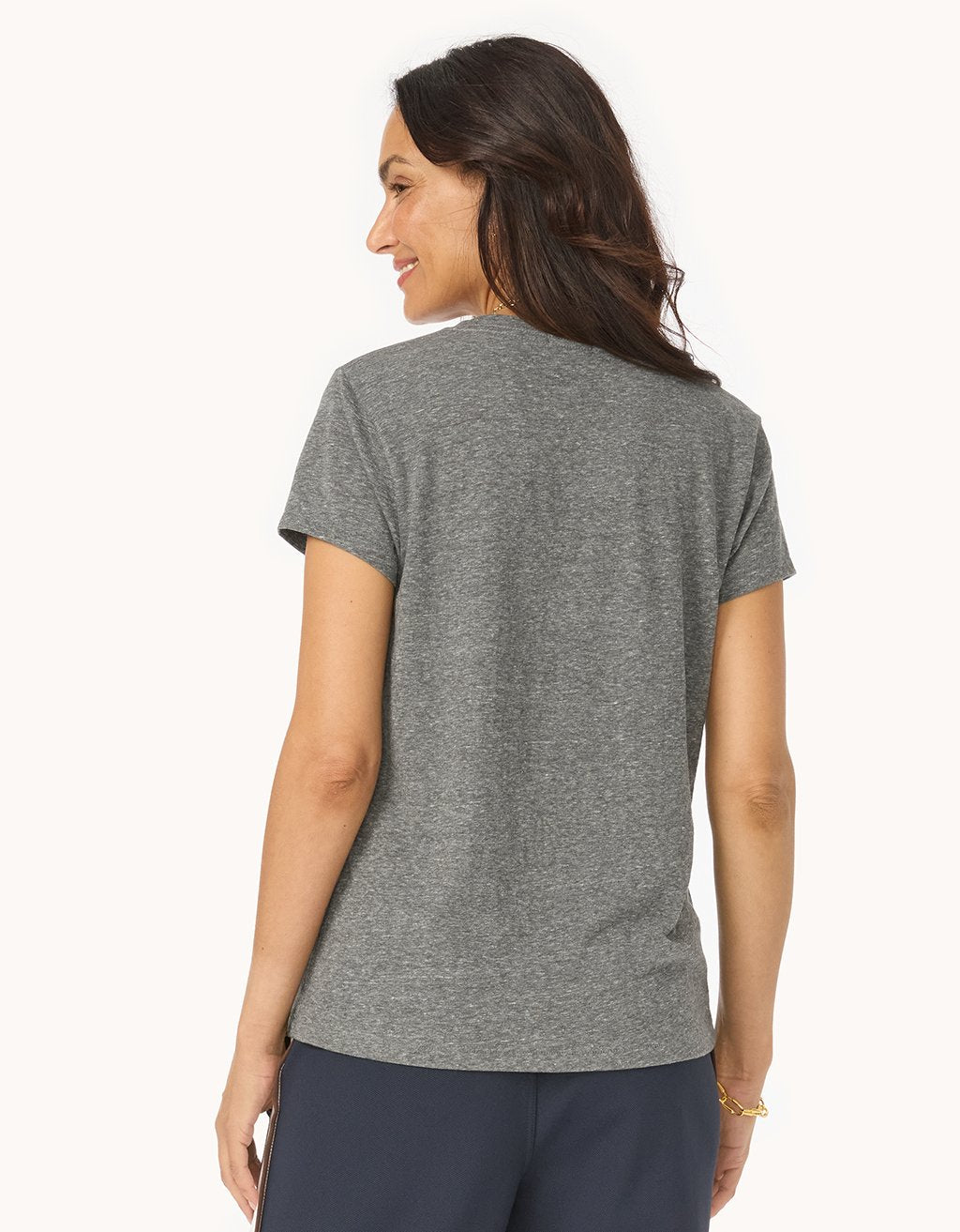 Back view of a woman wearing a heather gray V-neck t-shirt and navy pants on a white background