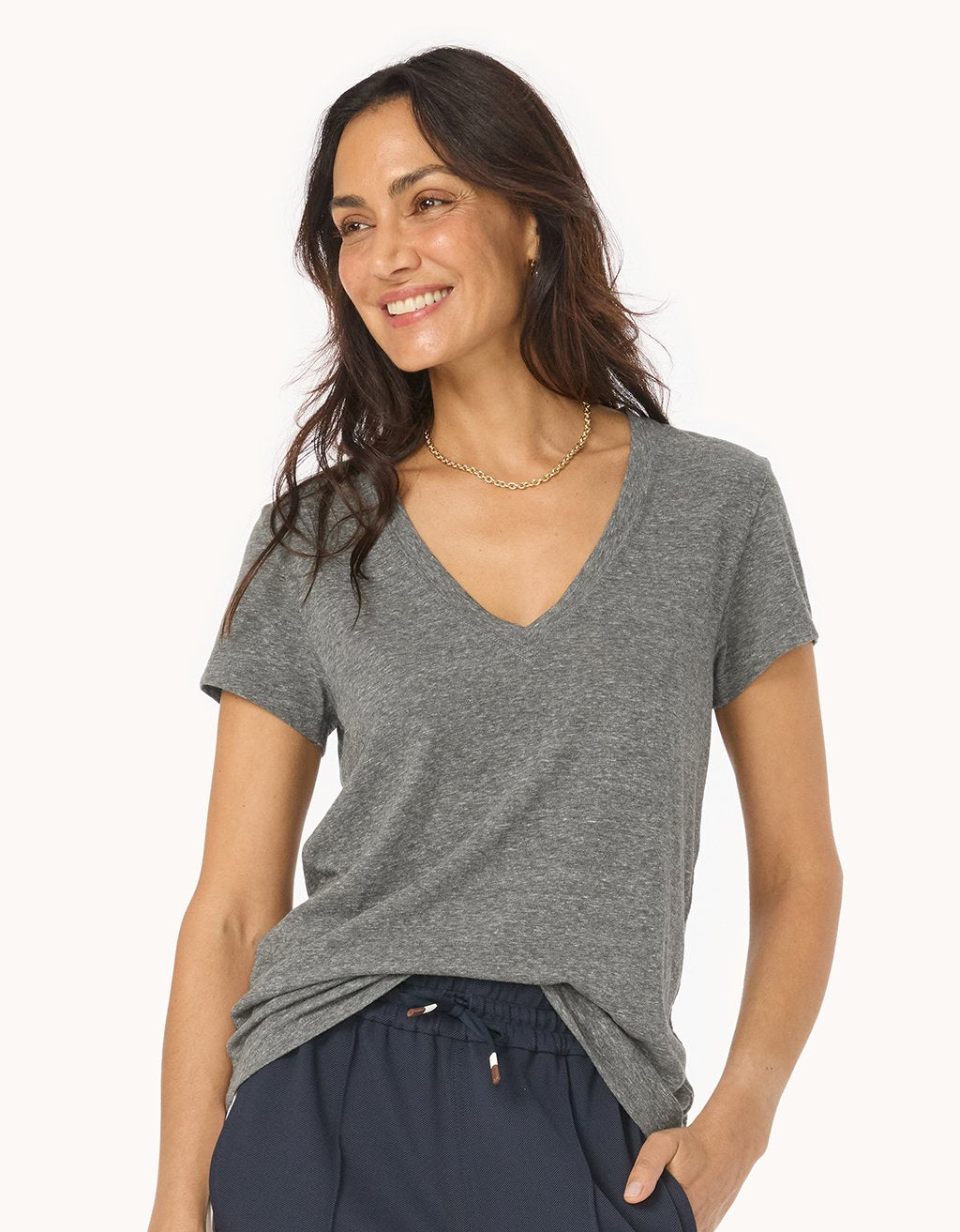 Woman wearing a heather gray V-neck t-shirt and navy pants on a white background
