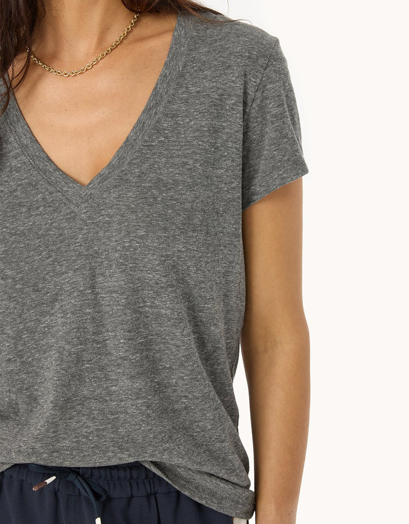 Close-up of a heather gray V-neck t-shirt and navy pants worn by a person on a white background