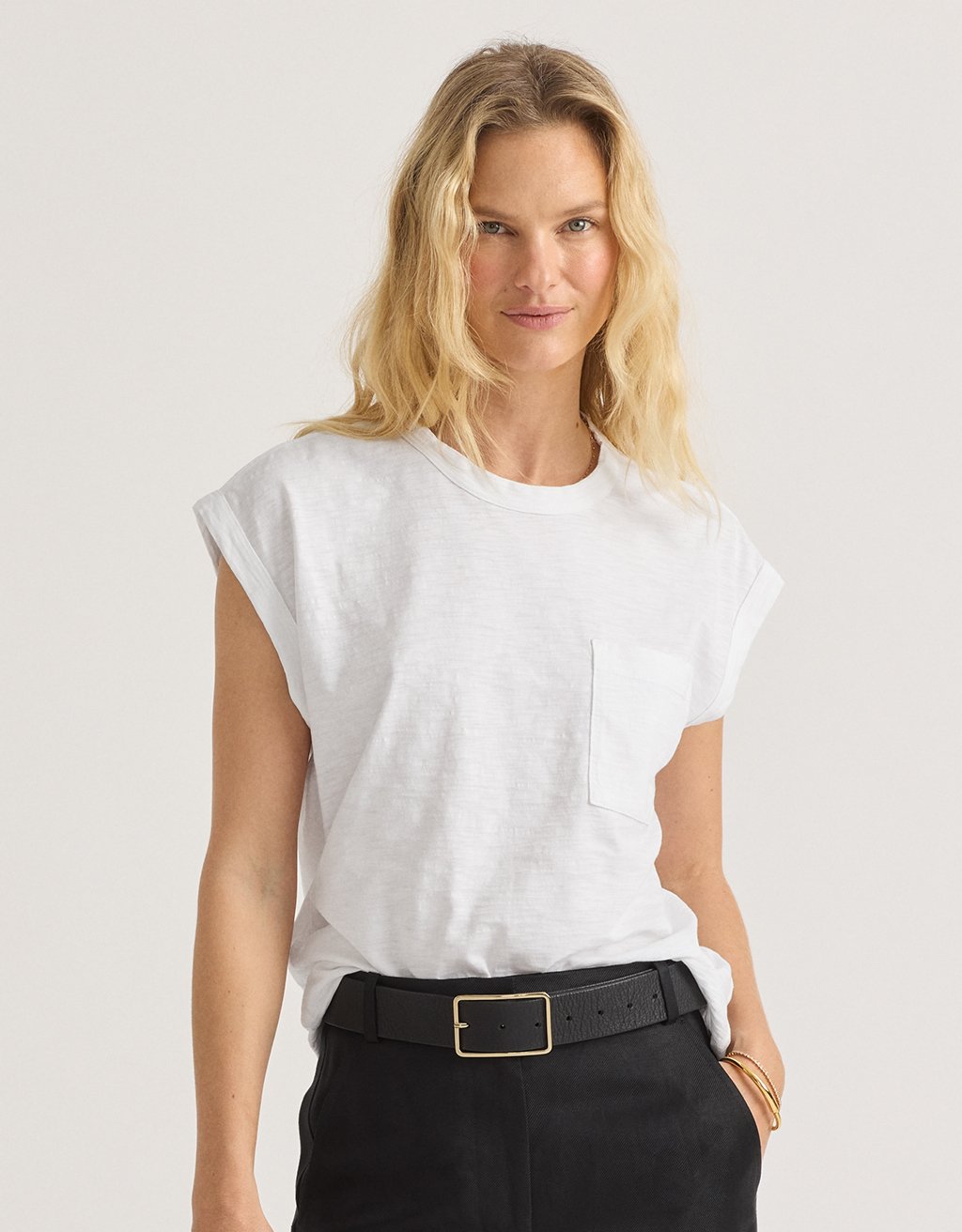 Woman wearing a white muscle t-shirt and black pants on a plain background