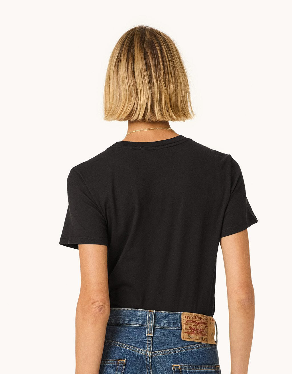 Back view of a person wearing a black t-shirt and blue jeans on a light gray background
