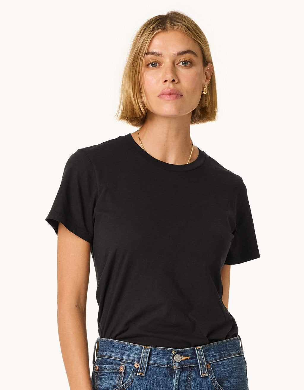Woman wearing a black t-shirt and blue jeans on a light gray background