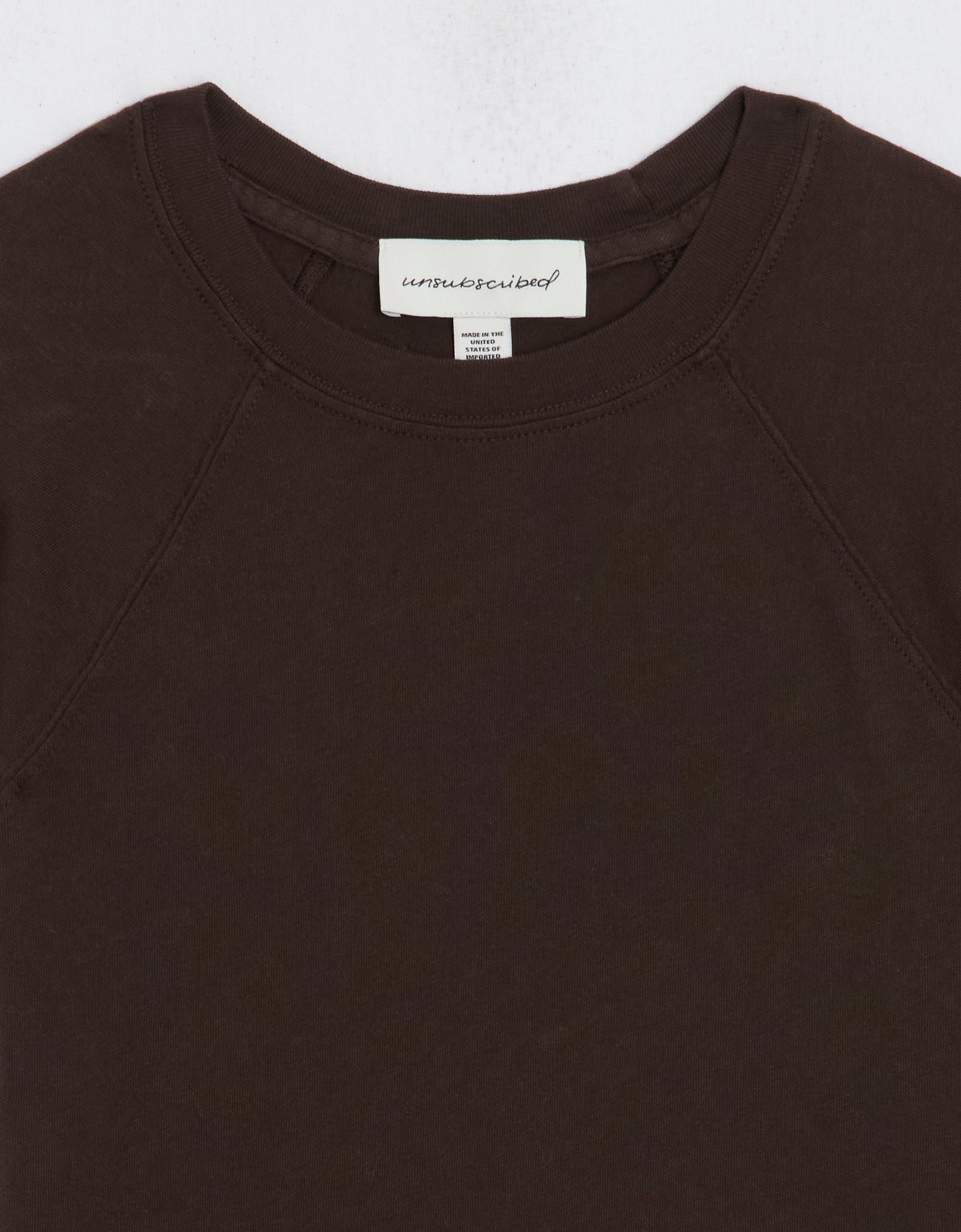 Close-up of a dark brown raglan t-shirt with a brand label on a light gray background