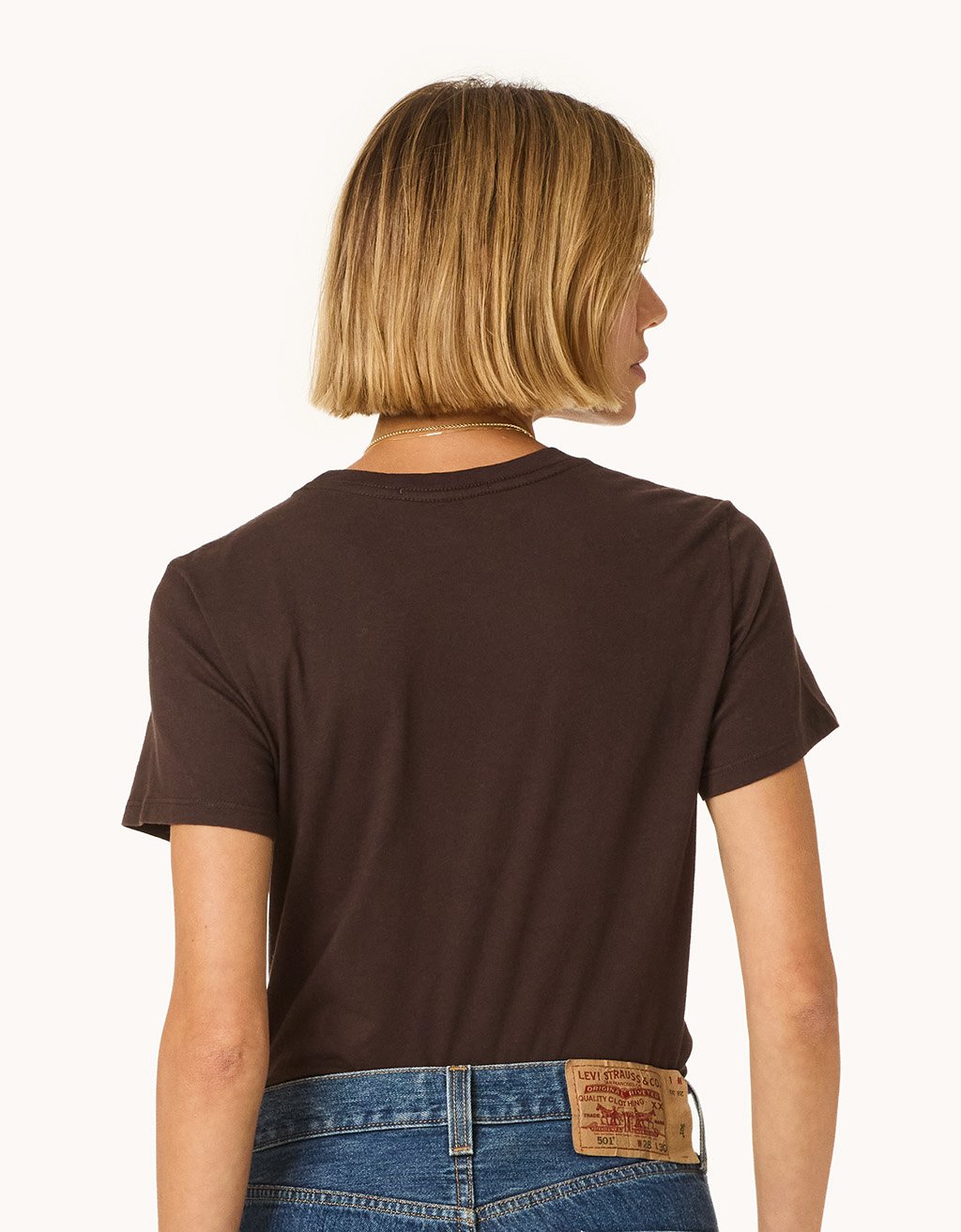 Back view of a person wearing a brown t-shirt and blue jeans on a light gray background