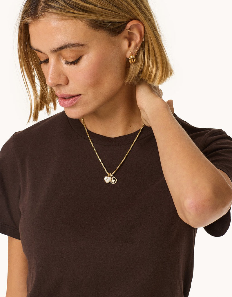 Woman wearing a brown t-shirt and gold charm necklaces on a light gray background