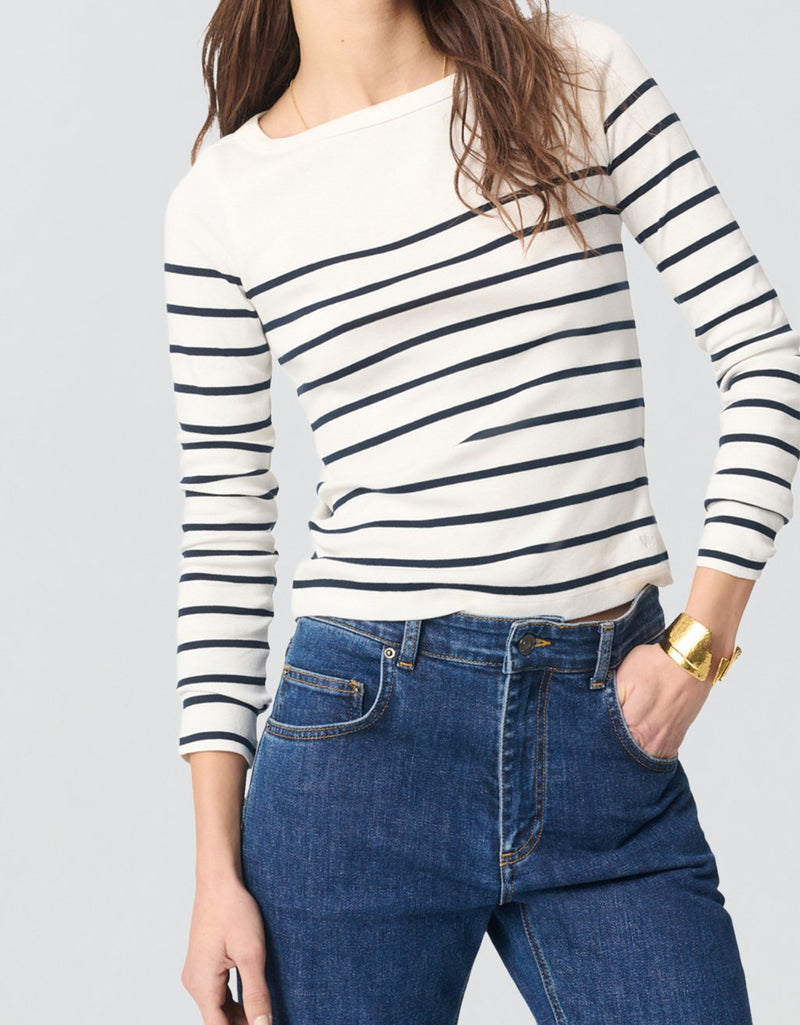 Woman wearing a striped long-sleeve top and blue jeans on a light gray background
