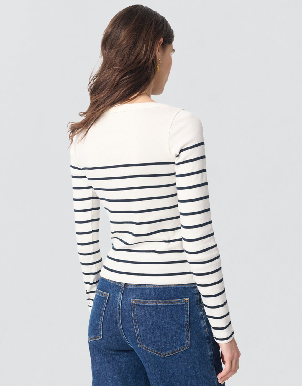 Back view of a woman wearing a striped long-sleeve top and blue jeans on a light gray background