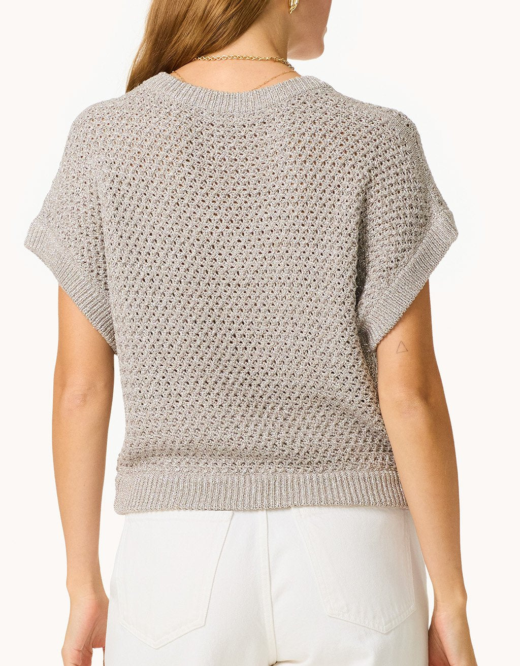 Woman wearing a silver open knit top with short sleeves on a plain background