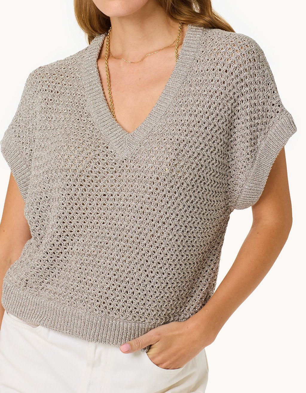 Woman wearing a silver open knit top on a plain background