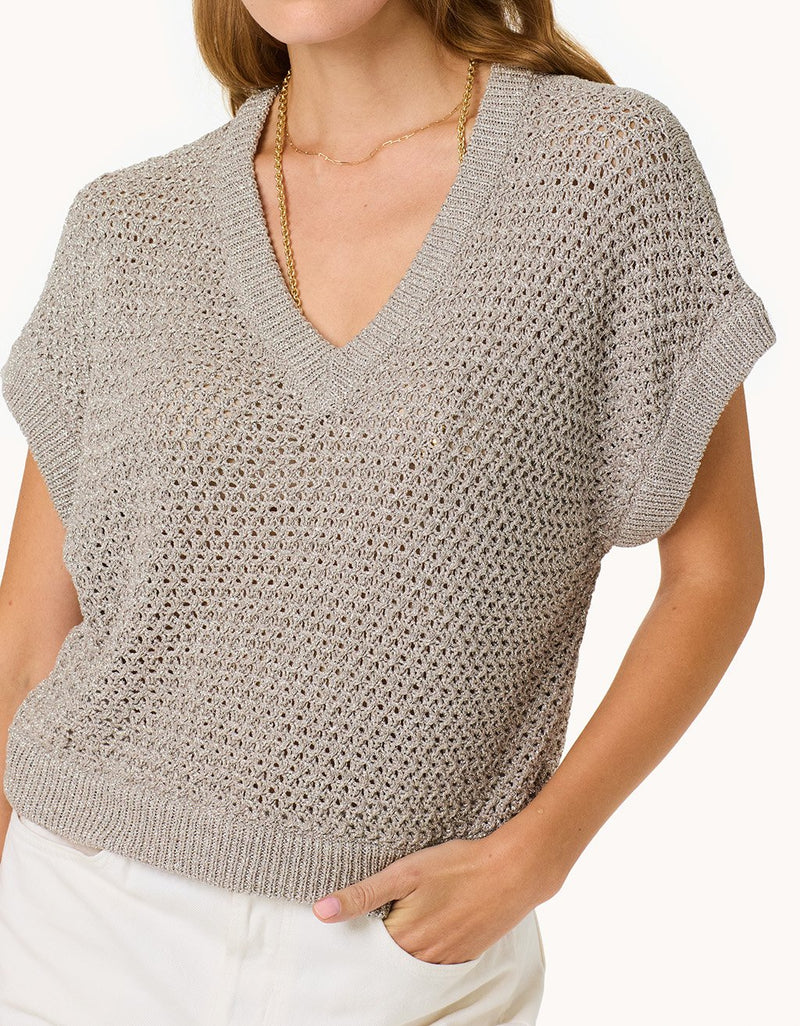 Woman wearing a silver open knit top on a plain background