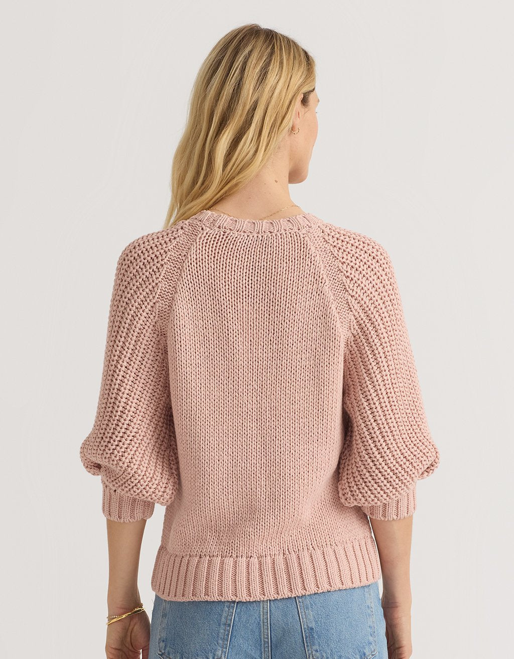 Back view of a woman wearing a pink puff sleeve sweater on a light gray background
