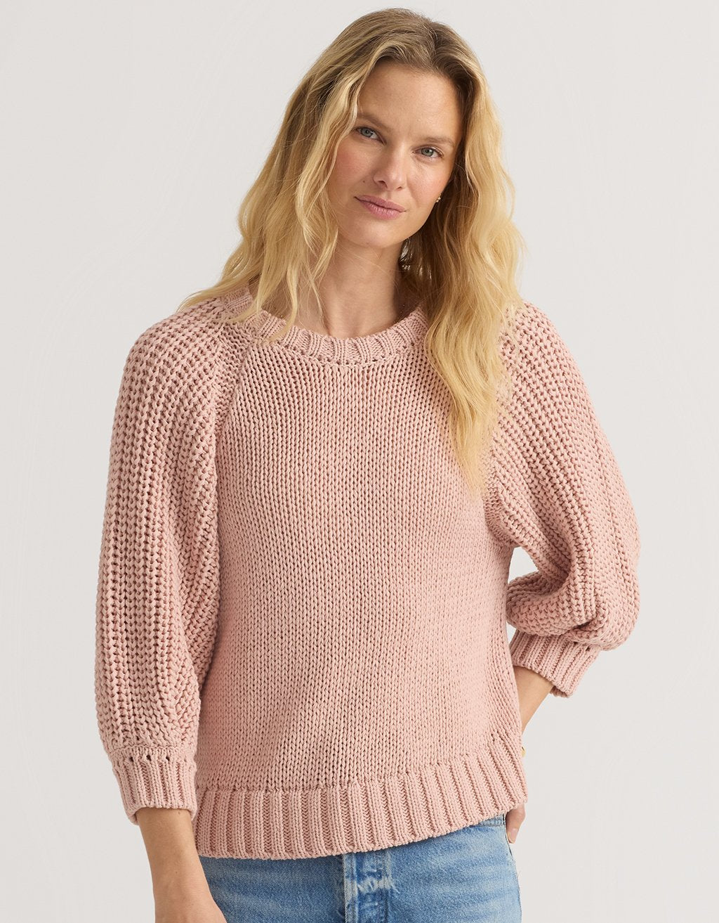 Woman wearing a pink puff sleeve sweater against a plain background