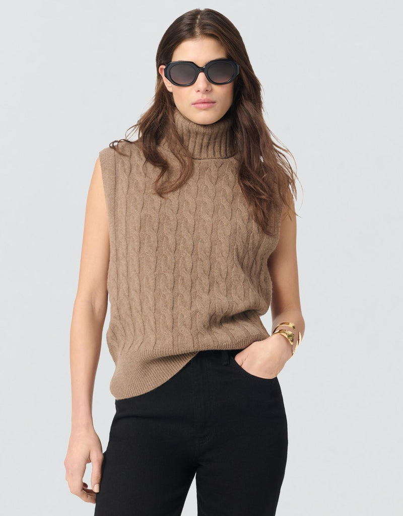 Woman wearing a camel sleeveless knit turtleneck sweater and sunglasses on a light gray background