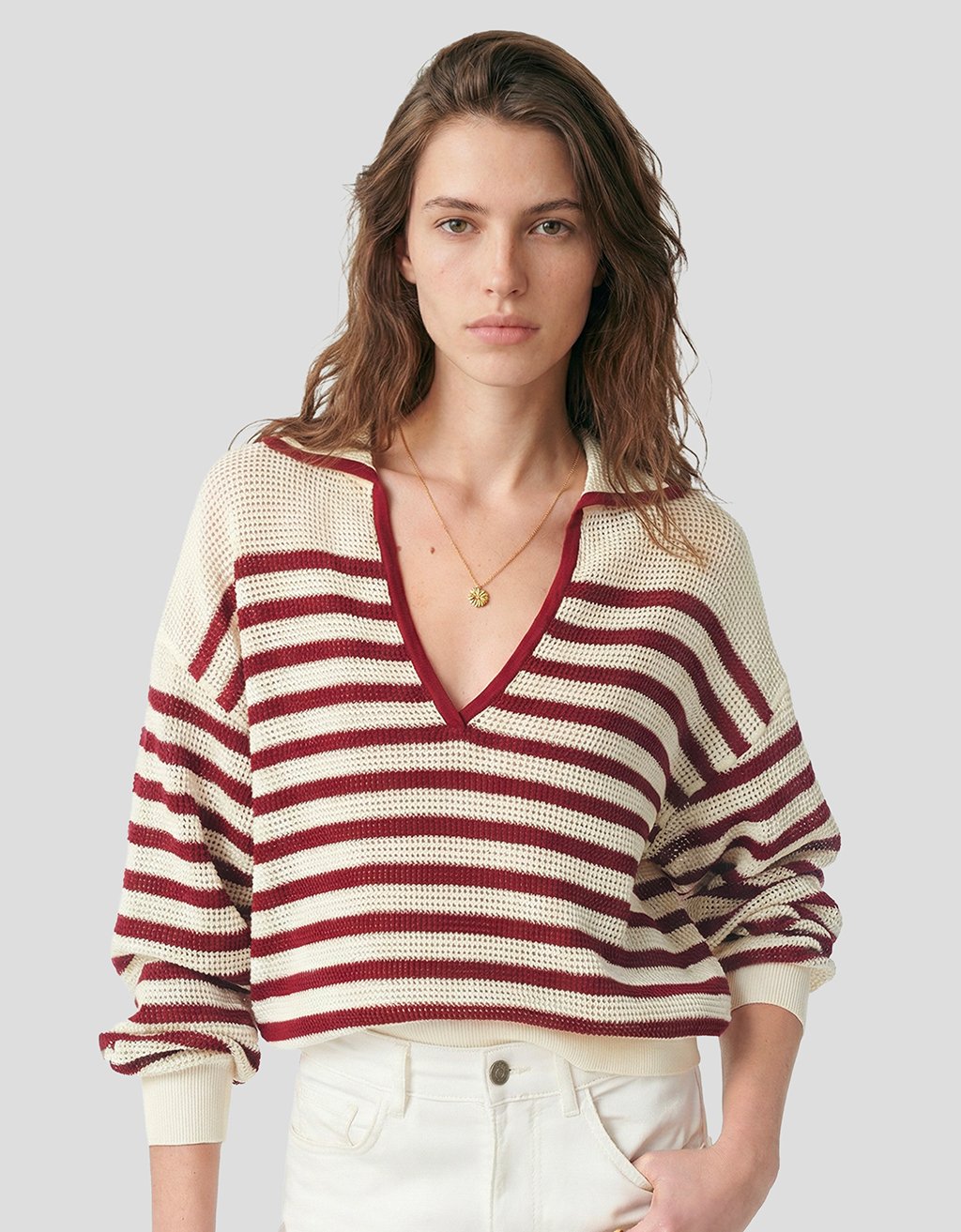 Person wearing an open knit cream sweater with red stripes and a deep V polo neckline on a light gray background
