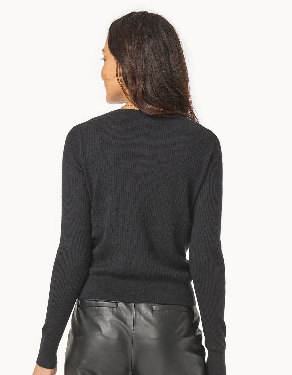 Back view of a woman wearing a black ribbed cashmere sweater and leather pants on a white background