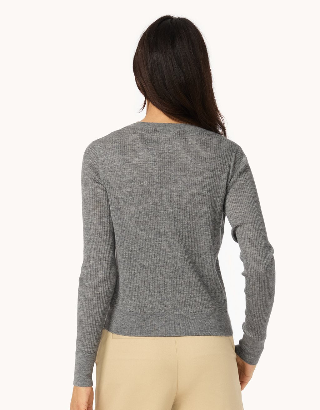 Back view of a woman wearing a gray ribbed cashmere cardigan and neutral pants on a white background