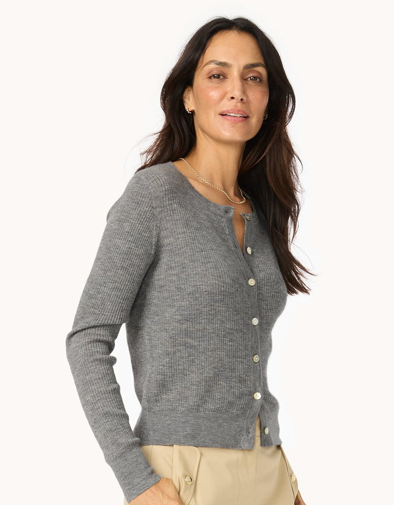 Woman wearing a gray ribbed cashmere cardigan and neutral pants on a white background