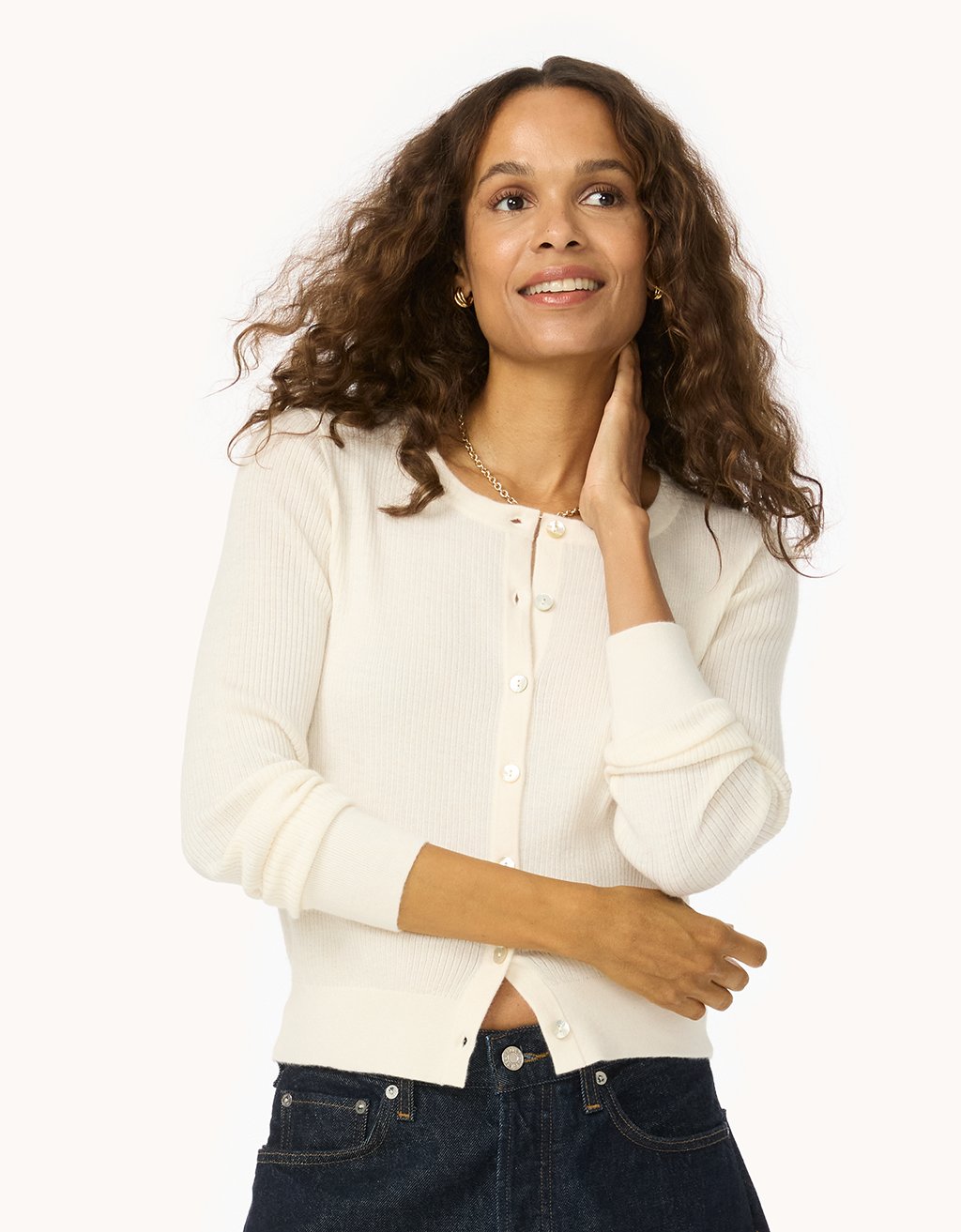 Woman wearing an ivory ribbed cashmere cardigan with dark jeans on a white background