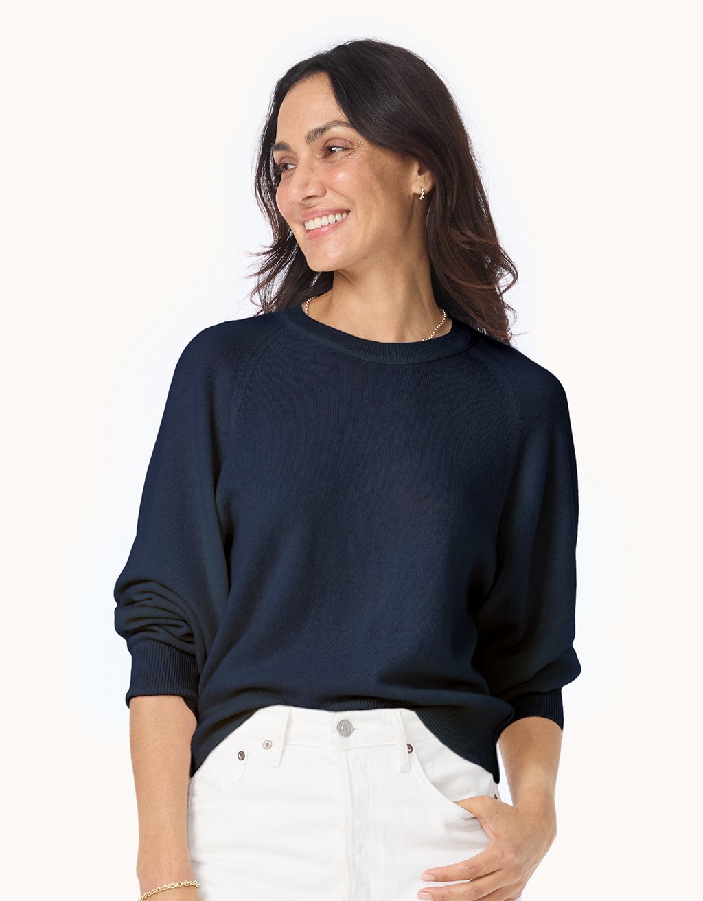 Woman wearing a navy cashmere raglan sweater and white jeans on a light gray background