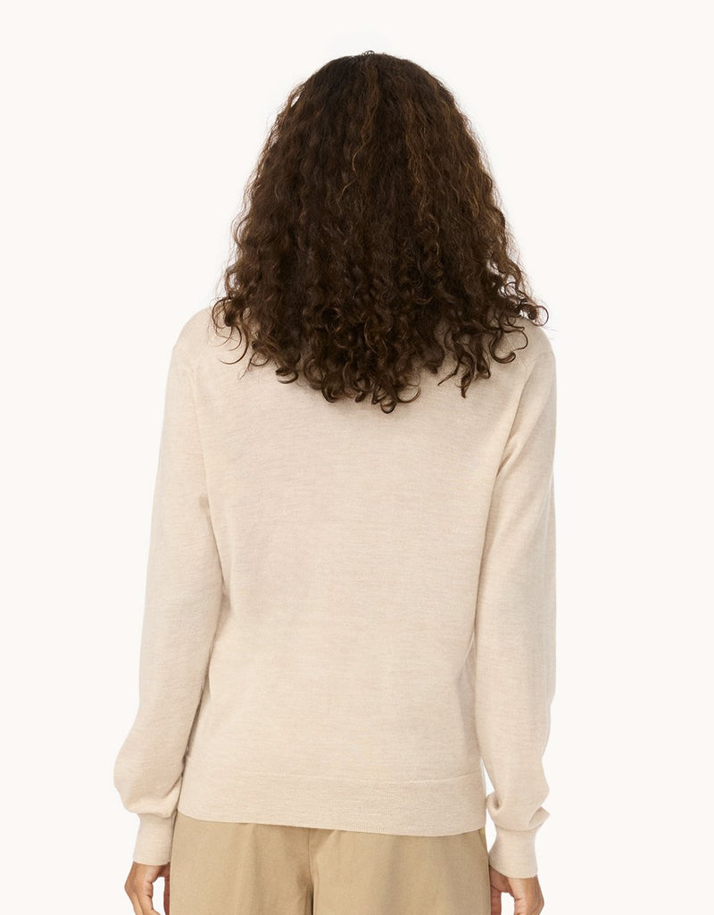 Back view of a woman wearing a beige cashmere sweater and pants on a light gray background