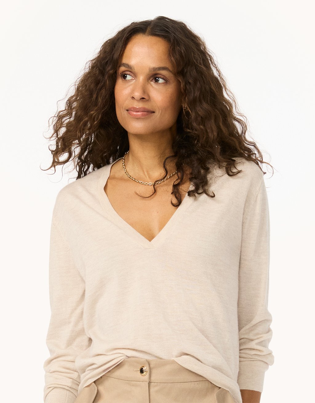 Woman wearing a beige cashmere V-neck sweater and pants on a light gray background