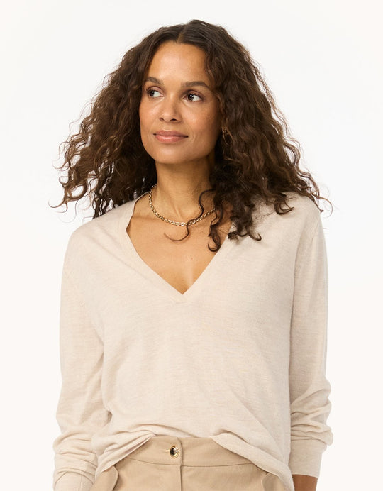 Woman wearing a beige cashmere V-neck sweater and pants on a light gray background