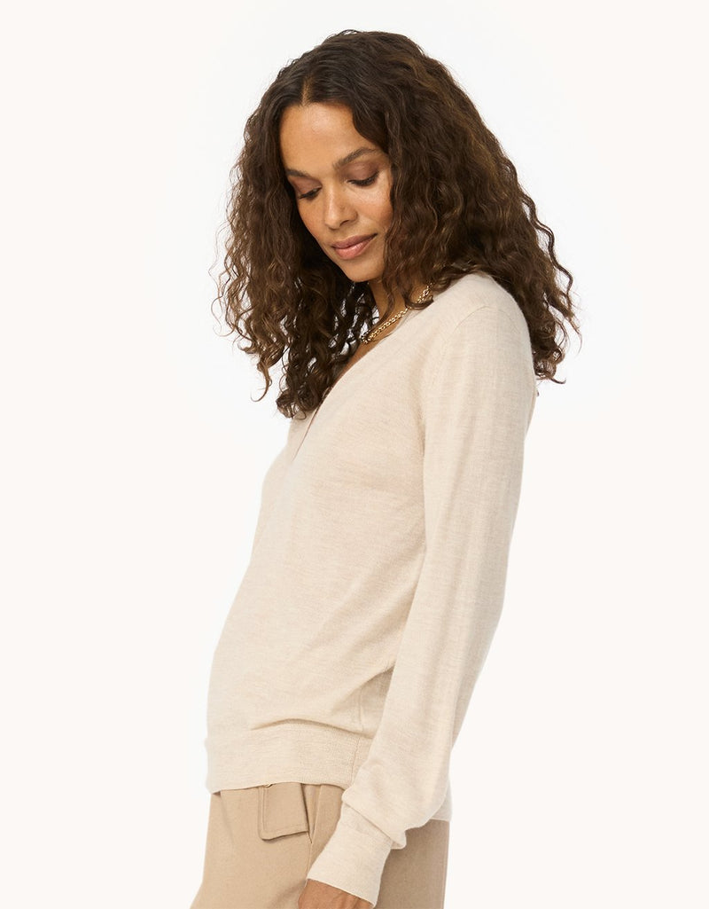 Side view of a woman wearing a beige cashmere sweater on a plain background