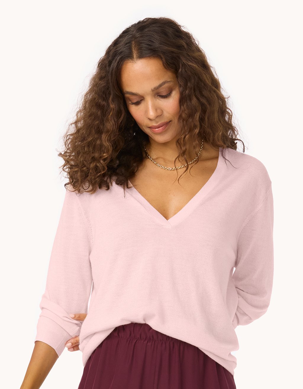 Woman wearing a light pink V-neck cashmere sweater and maroon pants on a white background