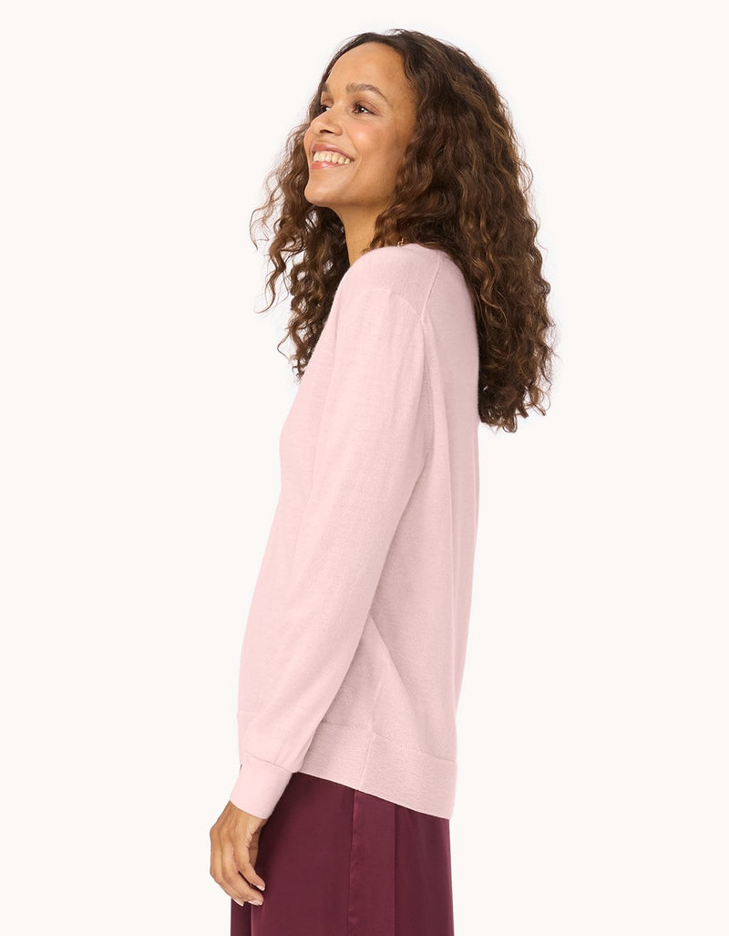 Profile of a woman wearing a light pink cashmere sweater with maroon pants on a white background