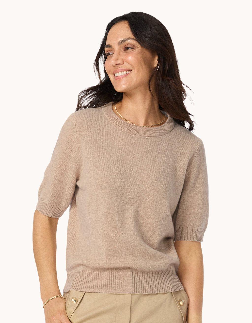 Woman wearing a camel cashmere sweater tee and neutral pants on a white background