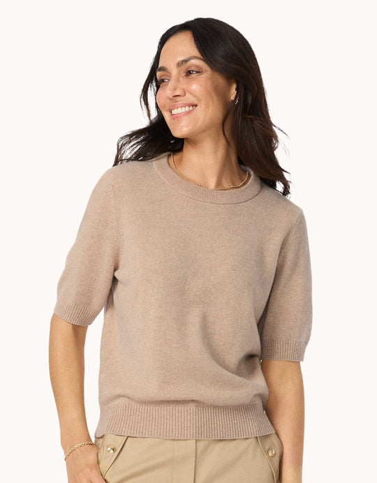 Woman wearing a camel cashmere sweater tee and neutral pants on a white background