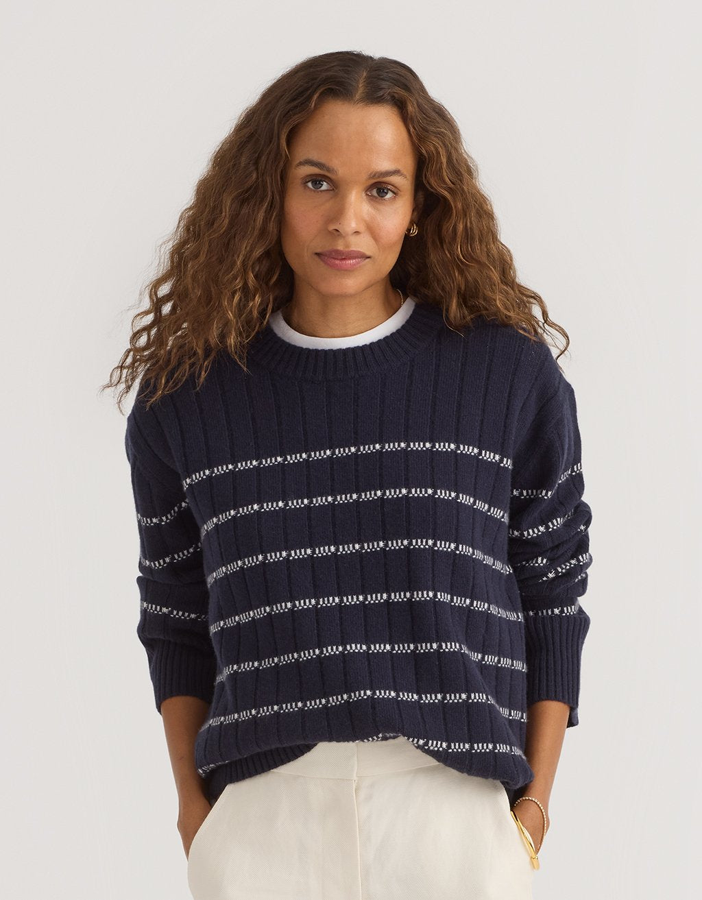 Woman wearing a navy cashmere ribbed stripe sweater on a plain background