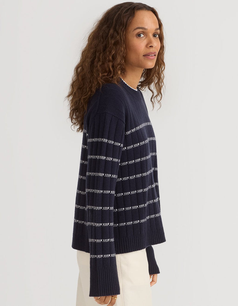 Woman wearing a navy ribbed cashmere stripe sweater on a plain background