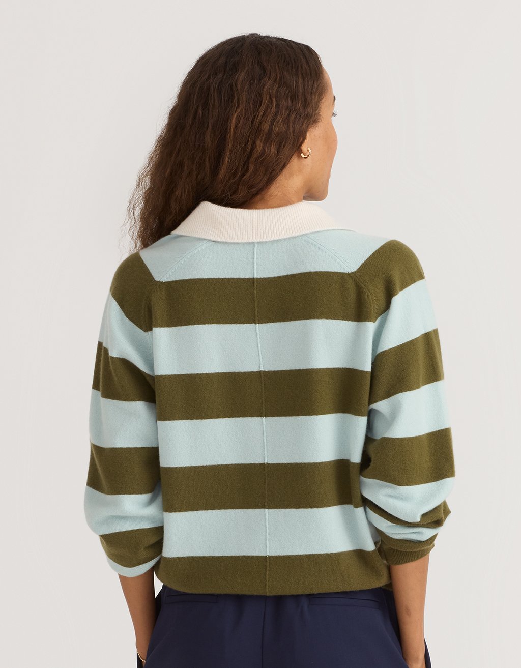 Back view of a woman wearing a green and light blue striped cashmere polo sweater on a plain background