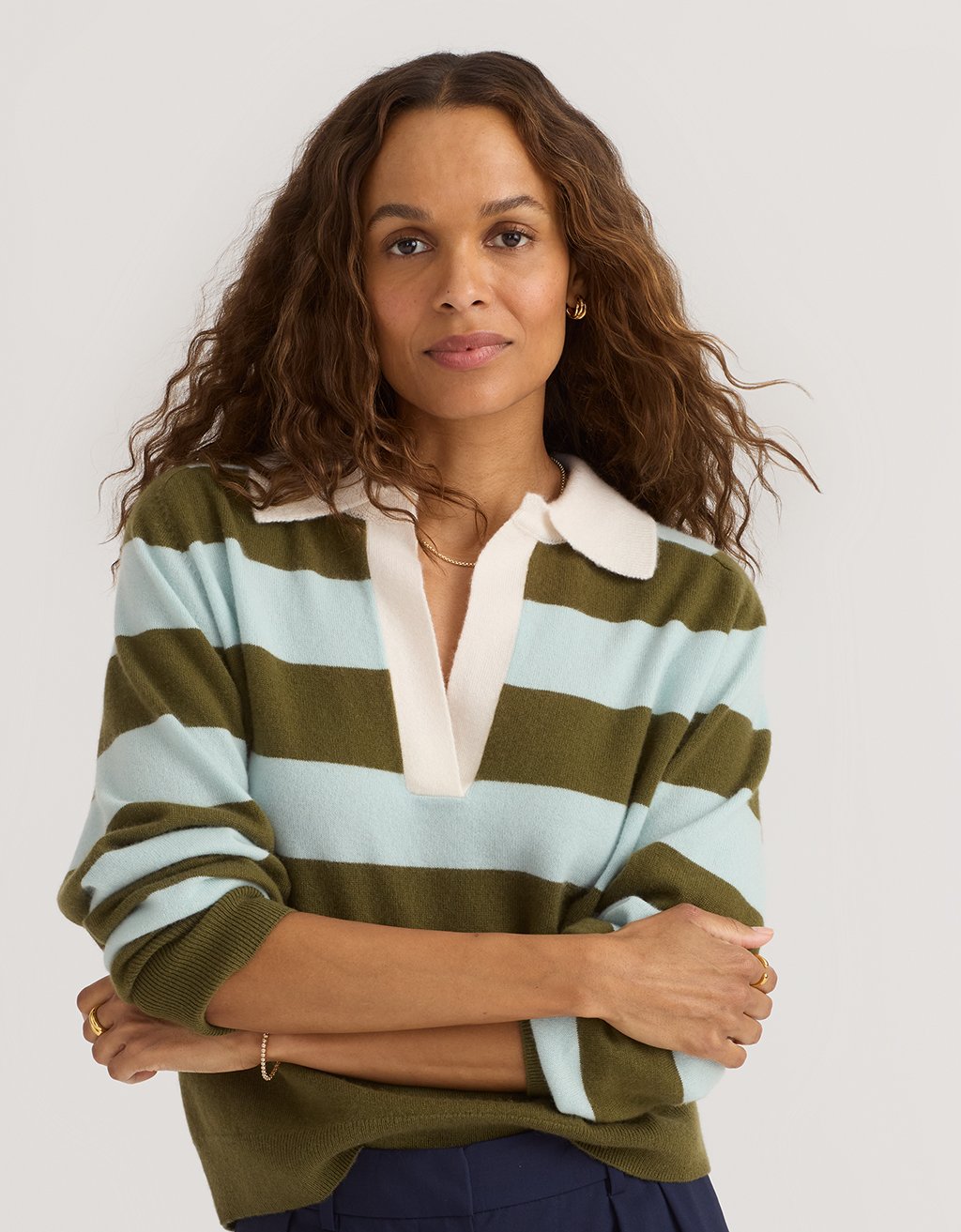 Woman wearing a green and light blue striped cashmere sweater with a white collar against a plain background