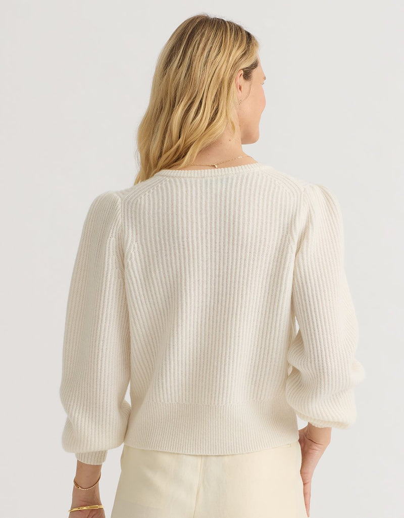 Back view of a woman wearing an ivory  cashmere puff sleeve cardigan on a light gray background
