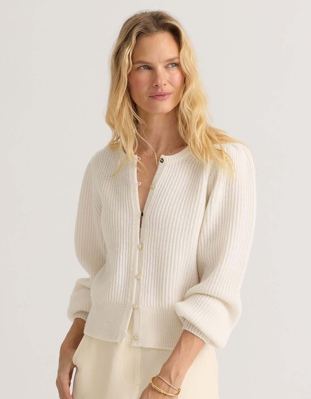 Woman wearing an ivory cashmere puff sleeve cardigan against a plain background