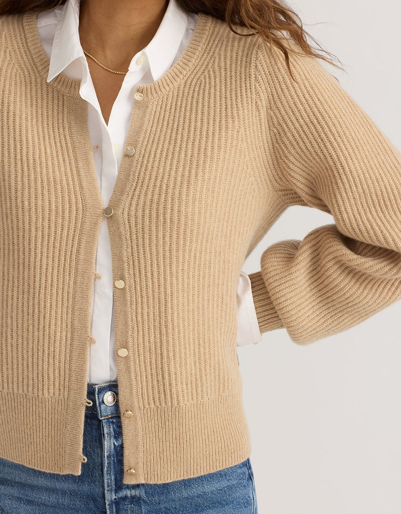 Close-up of a woman wearing a camel cashmere puff sleeve cardigan over a white shirt with a neutral background