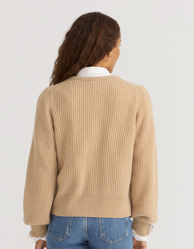 Back view of a woman wearing a camel cashmere puff sleeve cardigan and blue jeans on a plain background