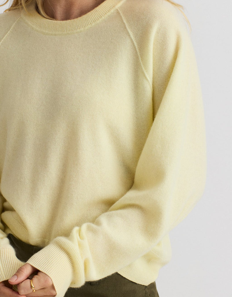 Close-up of a person wearing a light yellow cashmere raglan sweater on a plain background
