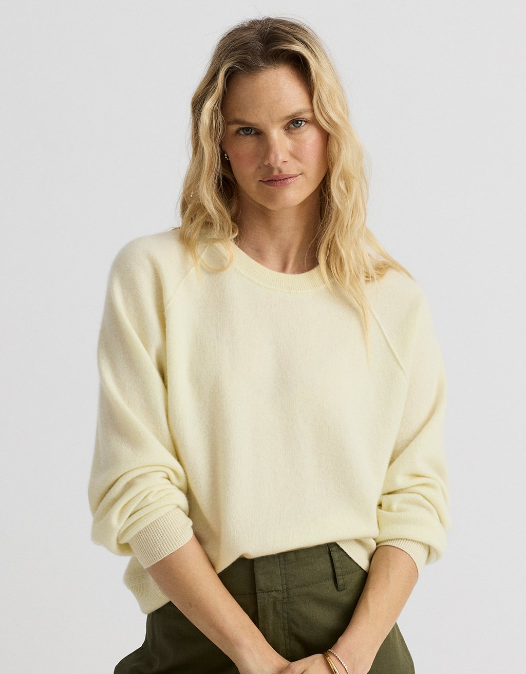 Woman wearing a light yellow raglan cashmere sweater on a light gray background