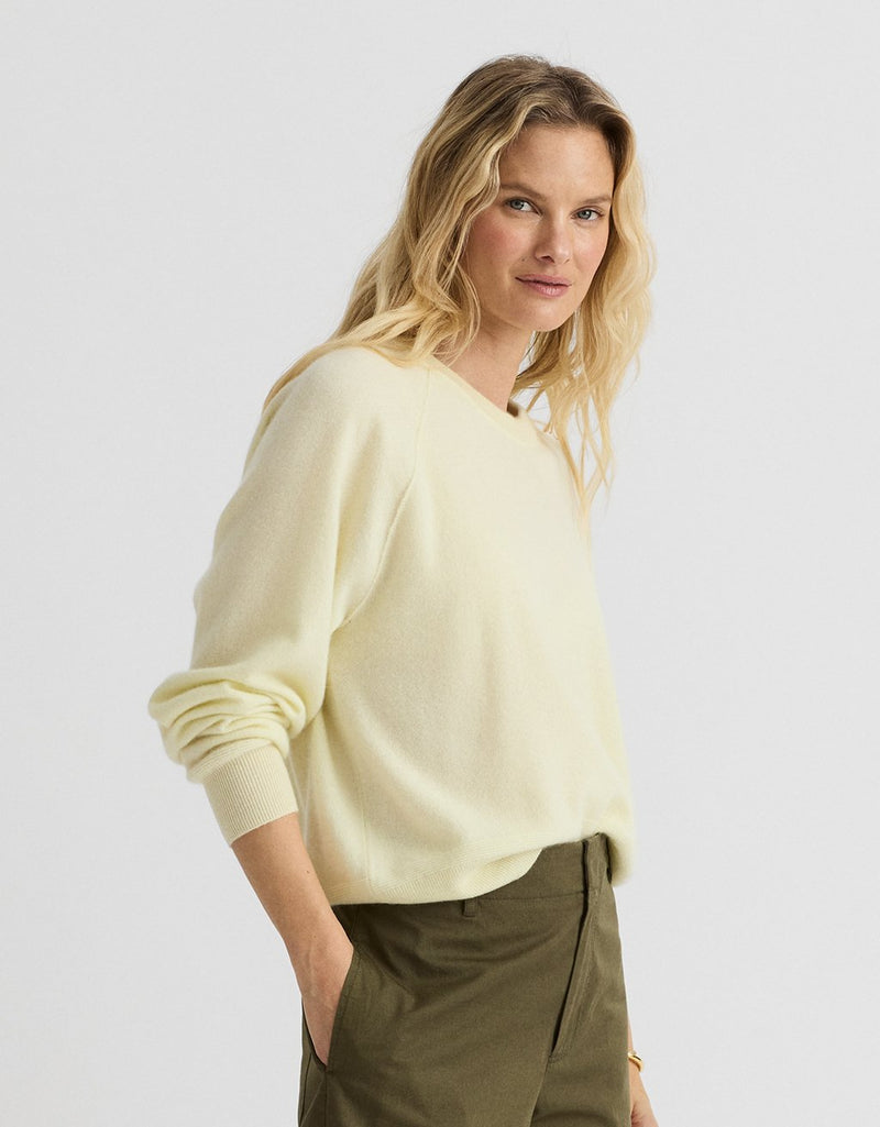 Woman wearing a light yellow cashmere raglan sweater and olive pants on a light gray background